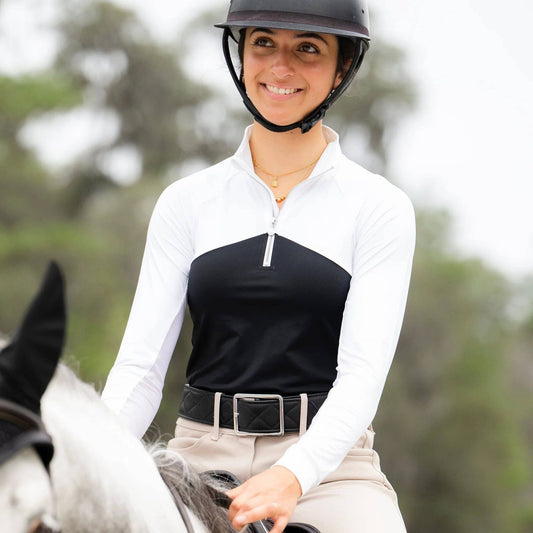 Woman riding a horse wearing a black and white equestrian outfit with a helmet.