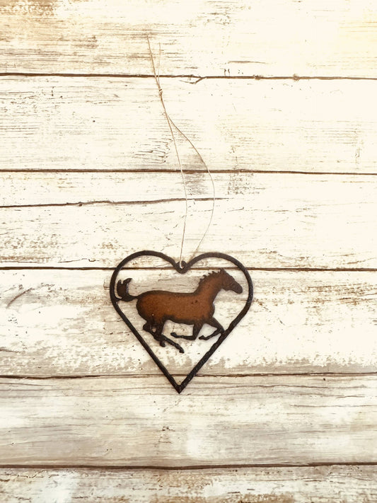 A rusted metal heart-shaped ornament with a horse silhouette in the center, hanging on a wooden fence.